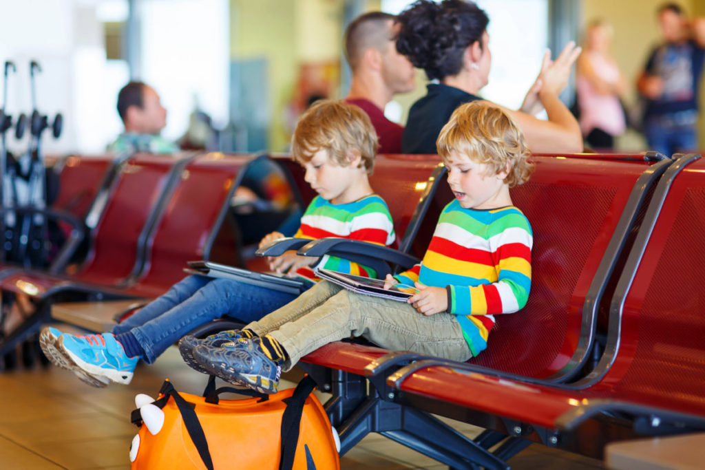 Two tired little sibling kids boys at the airport, traveling together. Upset children waiting and playing with tablet pc. Canceled flight due to pilot strike.